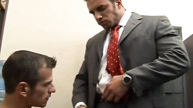Suited muscled boss unzips pants for kneeling cocksucker in gay office porn