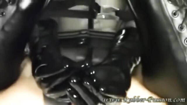 Rubber slave in latex catsuit and boots, gloved hands over crotch in BDSM tease