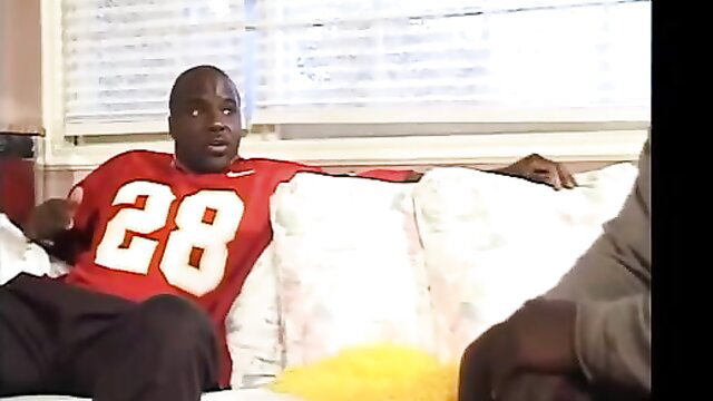 Black man in red #28 jersey lounging on couch in African Cheerleader adult video
