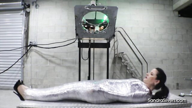 Sandra Silvers mummified in silver wrap, high heels, tickle BDSM pose