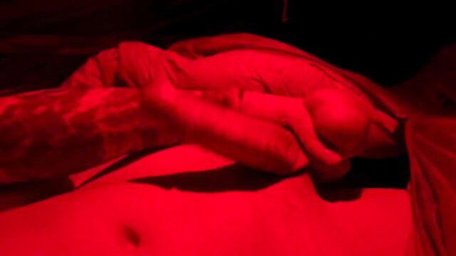 Red-lit closeup of nude woman cradling baby-like figure in intimate embrace