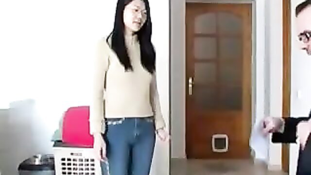 Asian woman in tight jeans stands by door in OTK spanking preview