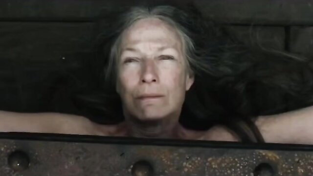 Grey-haired mature MILF bound topless in iron restraint public BDSM execution