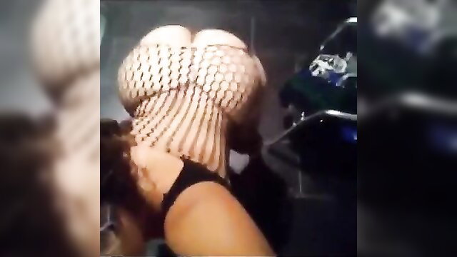 Busty woman in fishnet corset top bending over motorcycle