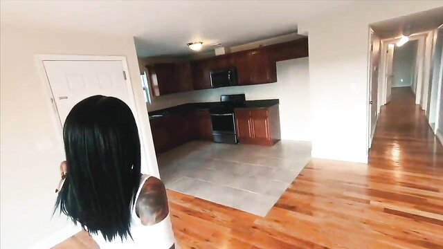 Black tattooed woman with long hair in tight white top tours apartment