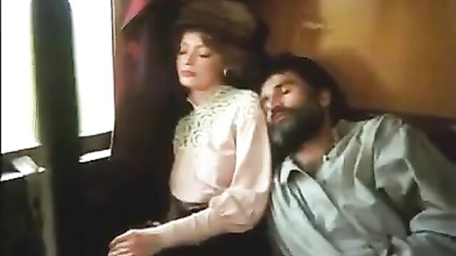 Retro 1983 Rasputin scene: busty brunette watches bearded man sleep in train