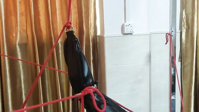 Asian woman in full black leather bondage suspended by red ropes BDSM