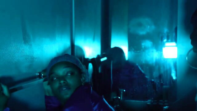 Sexy ebony MILF in purple outfit holding pipe in dark neon-lit scene