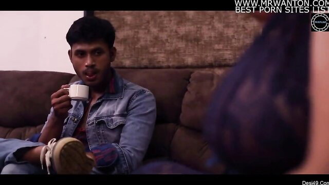 Indian guy sips tea on sofa as busty aunty in purple lingerie teases