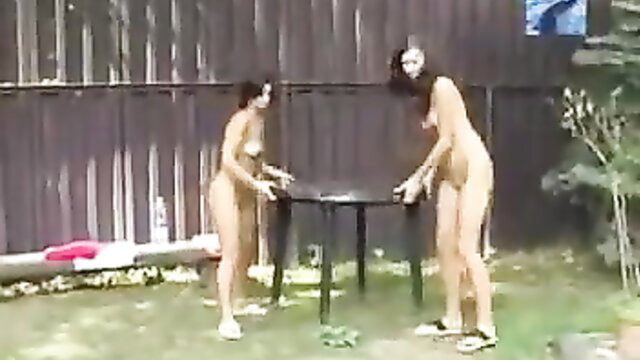 Two nude brunettes bending over table in voyeur nudist pool outdoor scene