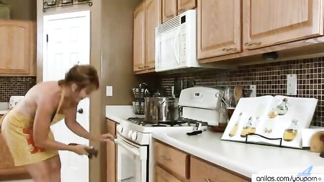 Mature redhead housewife in apron bends over kitchen counter