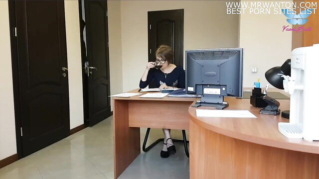 Sexy brunette secretary sips coffee at office desk in blouse and heels