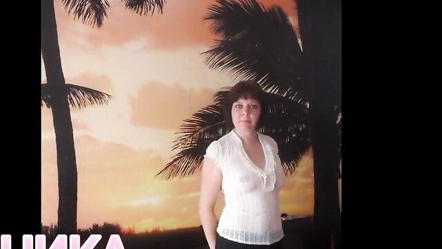 Brunette mature woman in sheer white blouse and black pants, tropical sunset backdrop