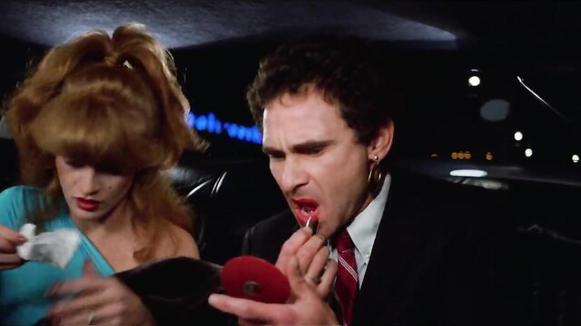 80s retro redhead applying lipstick to man's lips in limo
