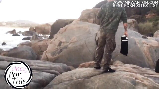 Joy Cardozo in military camo outdoors by rocks, public fetish tease