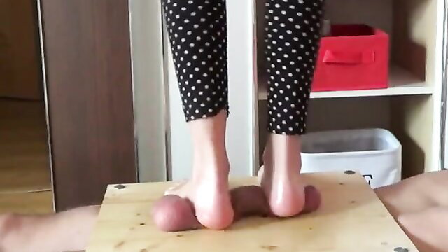 Barefoot girl in polka dot leggings tramples bound man's balls on wooden platform