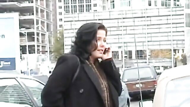 Brunette MILF in black coat on phone in urban street