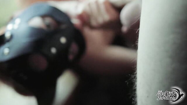 Blonde in mask kneels fellating cock, swallows cum closeup