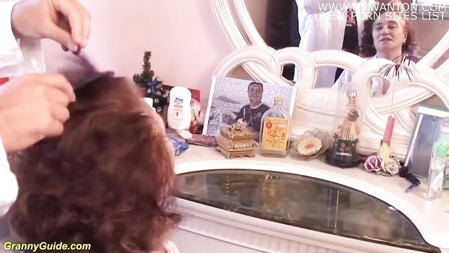 Grandma at vanity mirror brushed by hairdresser in salon scene