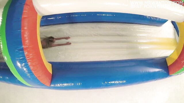 Slim Asian woman sliding nude down inflatable slide in playful adult fun