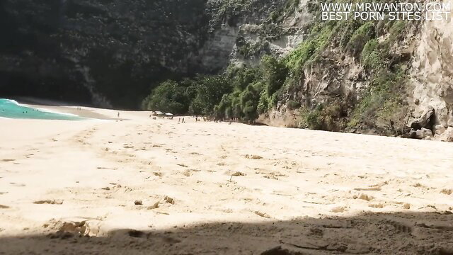 Tropical beach with white sand, turquoise water, cliffs, greenery and distant people