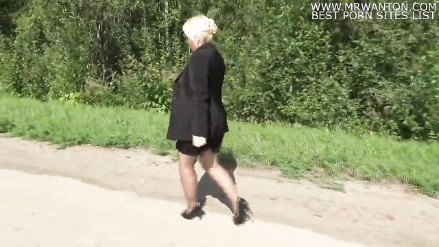 Blonde business lady in skirt suit and heels walks outdoors in forest