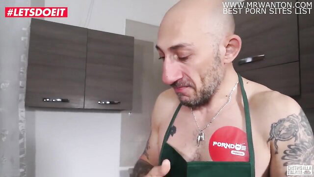Bald muscular guy in apron with PornDude badge on LetsDoeIt casting thumbnail