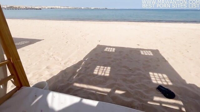 Sunny beach scene with white cabana shadows on sand, flip flop and sea view