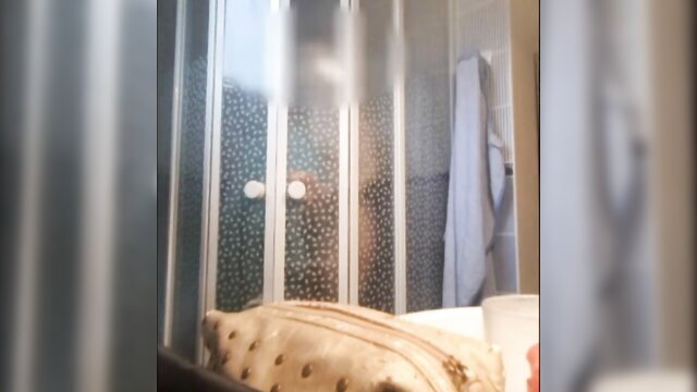 Blurry shower door with nude silhouette, towel and bag nearby