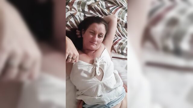 Amateur wife in open blouse and denim shorts lounging seductively on bed