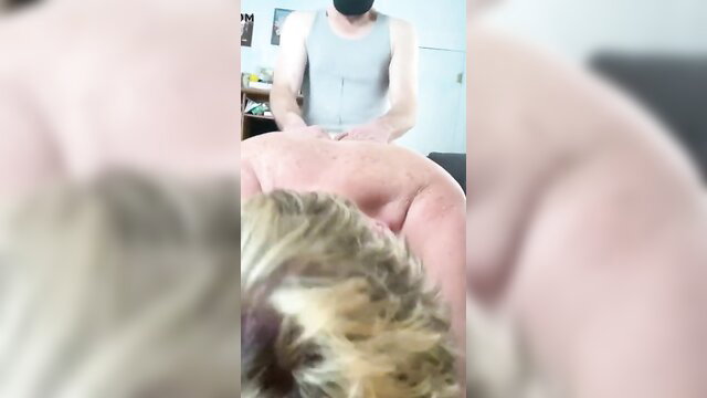 Blond guy bent over in tank top, masked man groping from behind in gay role play
