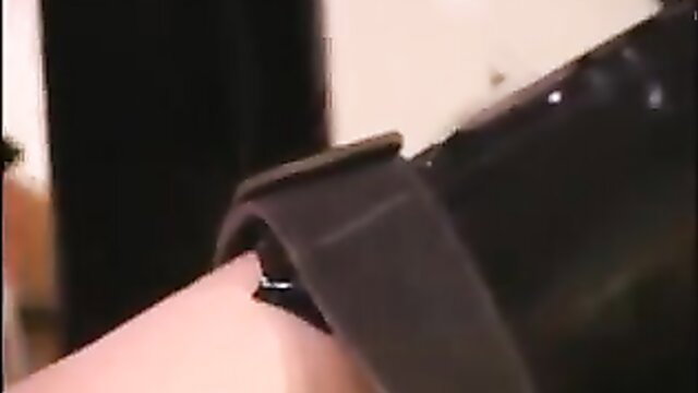 Rubber sex slave in black latex strap harness on pale arm closeup