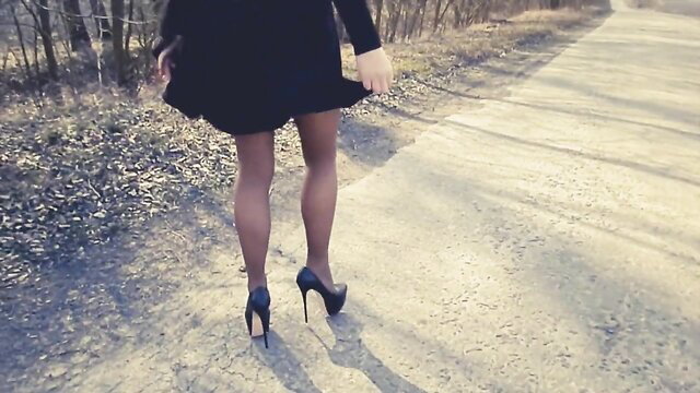 Woman walks on road in short black dress, nylons, high heels