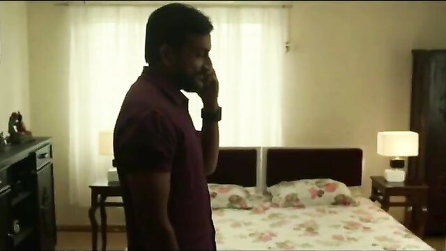 Indian man in maroon shirt on phone by bed in steamy bedroom scene