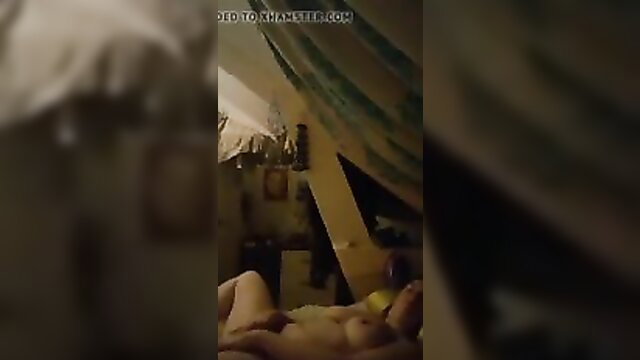 Nude woman lying on bed masturbating in dim attic room