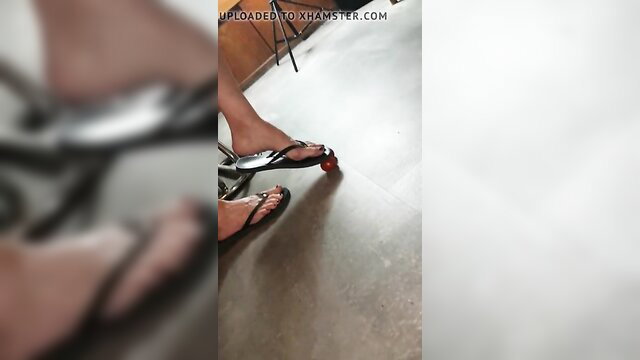 Barefoot woman in black flip flops crushing red tomato on floor