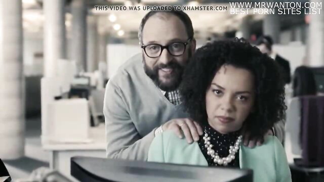 Balding man embraces curly-haired black woman at office desk