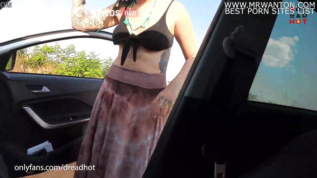 Tattooed brunette in bikini top and skirt posing by car on sunny road