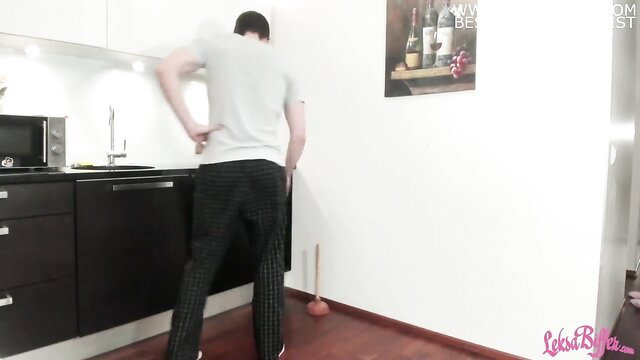 Fit plumber in grey tee and pants bending over in kitchen