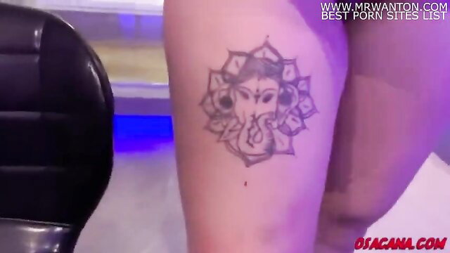 Closeup of woman's thigh with intricate Ganesha mandala tattoo in blue-lit room