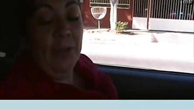 Mature Latina woman in car, red top, blurred face outdoor view