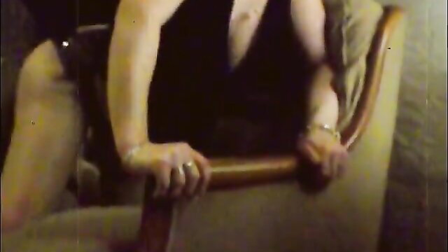 Blonde MILF in deep V dress gripping chair arms seductively