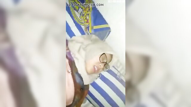 Malay hijab girl smiling shyly in bed, glasses on, teasing reveal