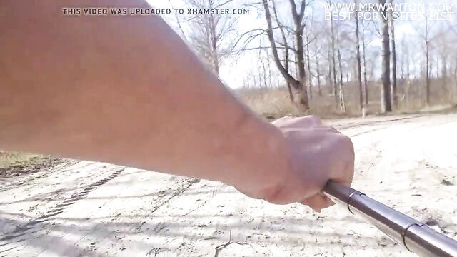 Nude woman gripping metal rod naked in forest trail, risky outdoor exposure