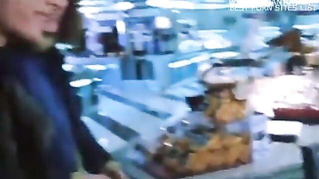 Blurry mature woman with long hair in store aisle grabs orange snacks