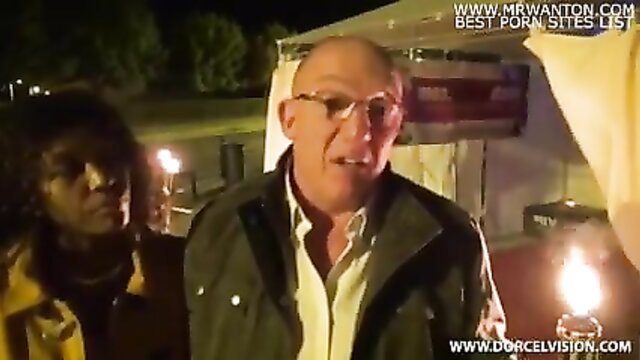 Bald man in jacket talks to black woman outdoors at night party