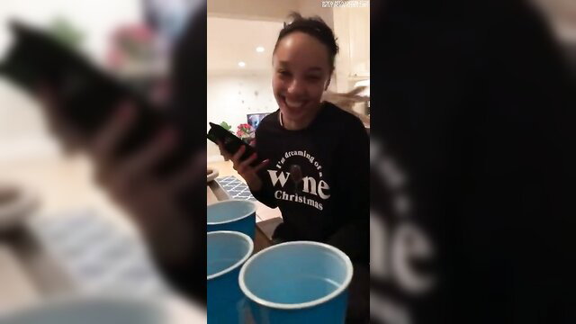 Smiling black woman in Xmas sweater holding phone at house party