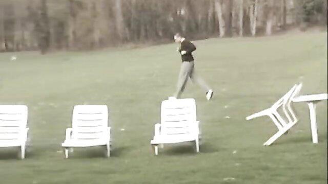 Brunette in grey tracksuit jumps over stacked chairs in outdoor Private lesson scene