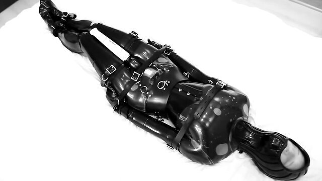 Bound latex sub in leather straps, gagged hood on BDSM table