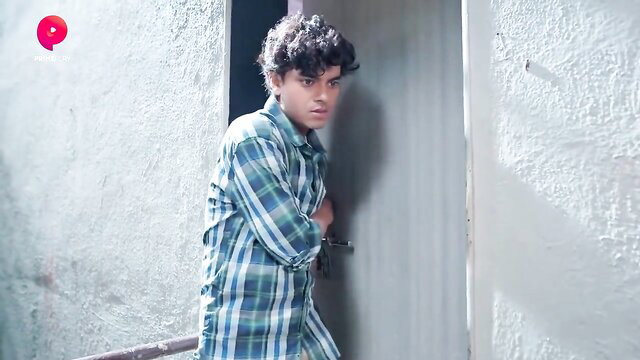 Young curly-haired Indian guy peeking from door in plaid pajamas
